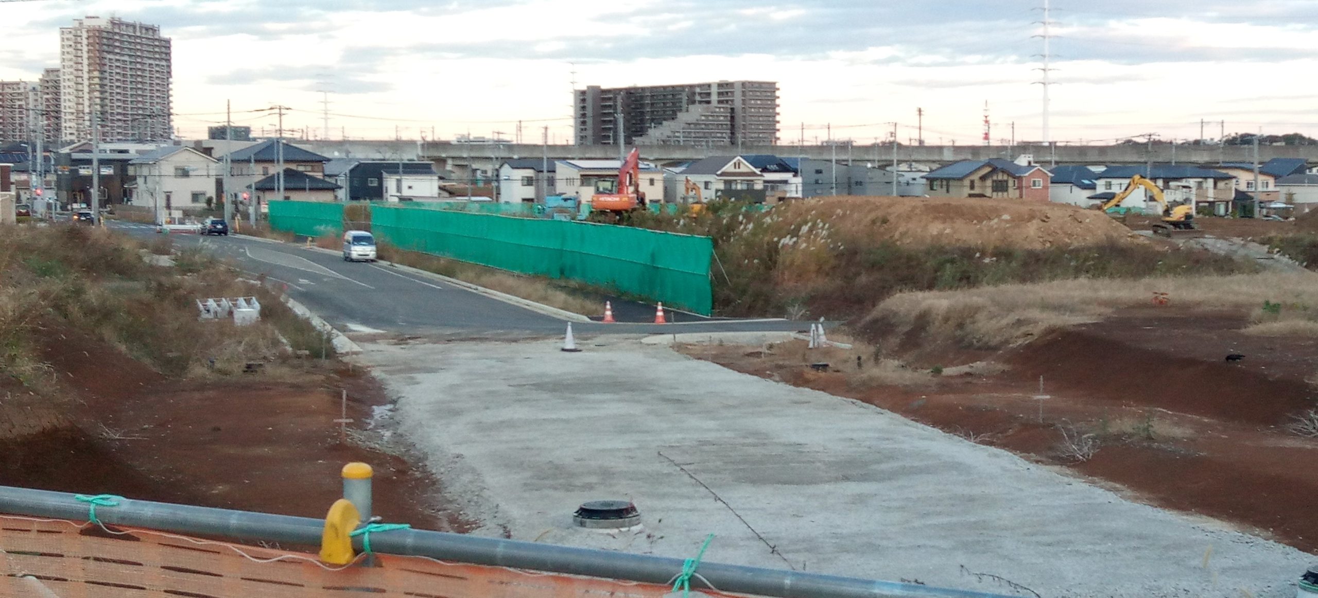 写真奥にＴＸの高架橋、左側奥がおおたかの森駅方面。マンションで、中央部分はスーパーヤオコー東側のマンション（ウエリスおおたかの森サウスアリーナ）。左側は駅南口そばのマンション（フォレストレジデンス）。写真下から左側へ走る道路は加市野谷線で、おおたかの森小中併設校・おおたかの森センターの前を通り、おおたかの森駅西口ロータリーへ抜ける道路。